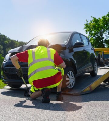Tow,Truck,Operator,Securing,A,Damaged,Car,On,A,Flatbed
